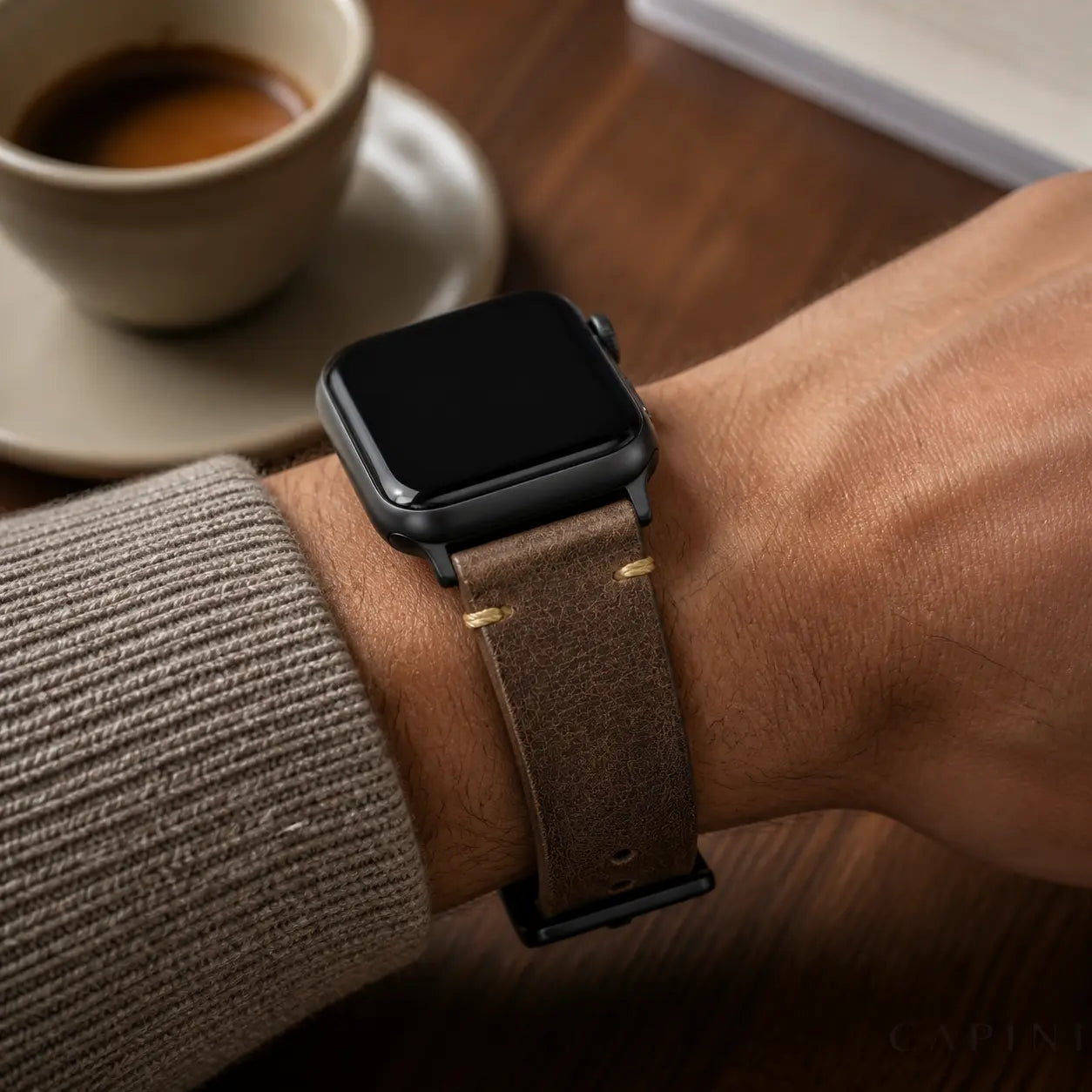 Coffee Trieste oil-wax Apple Watch strap with black hardware worn at a cafe