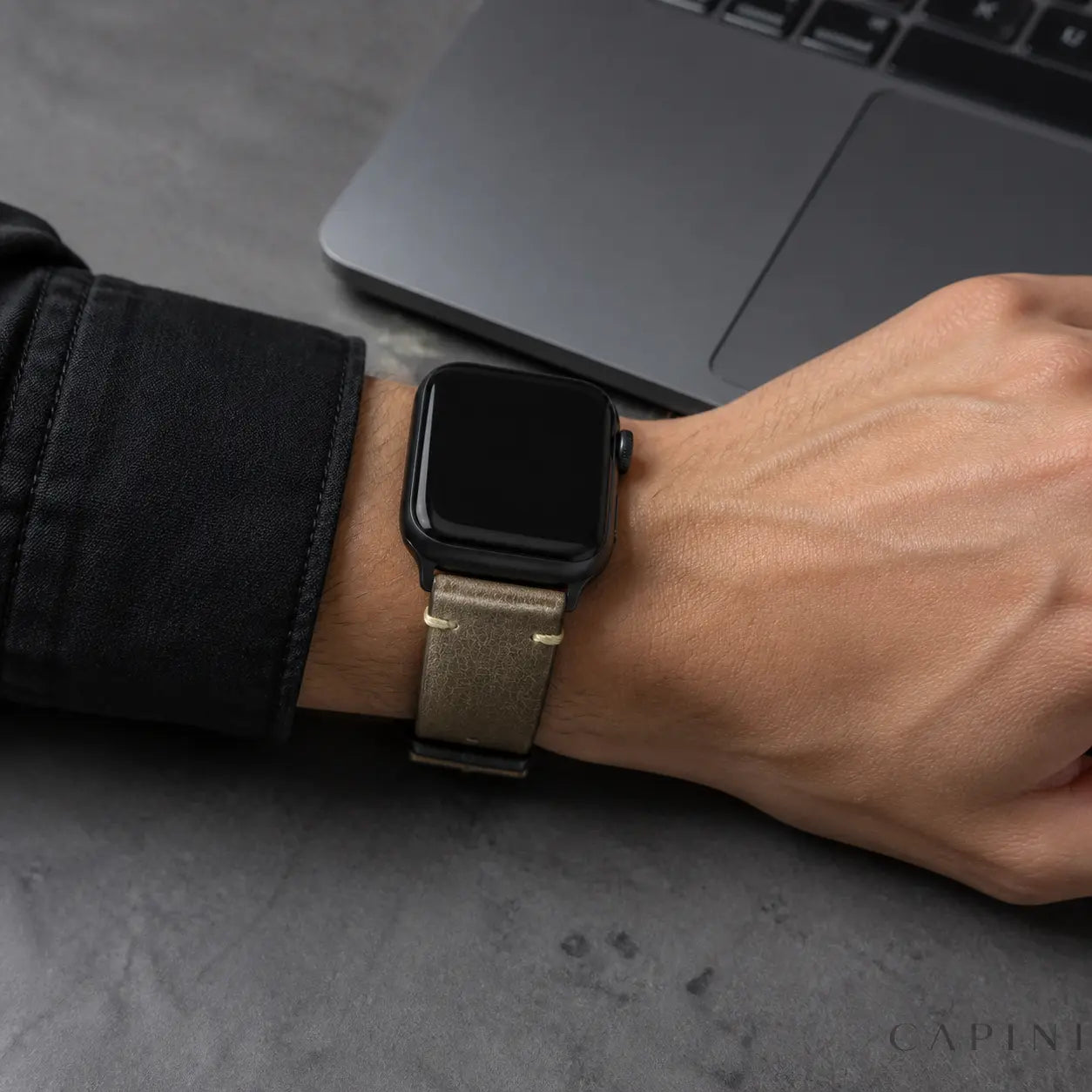 Gray Trieste oil-wax Apple Watch strap with black hardware worn at a modern office