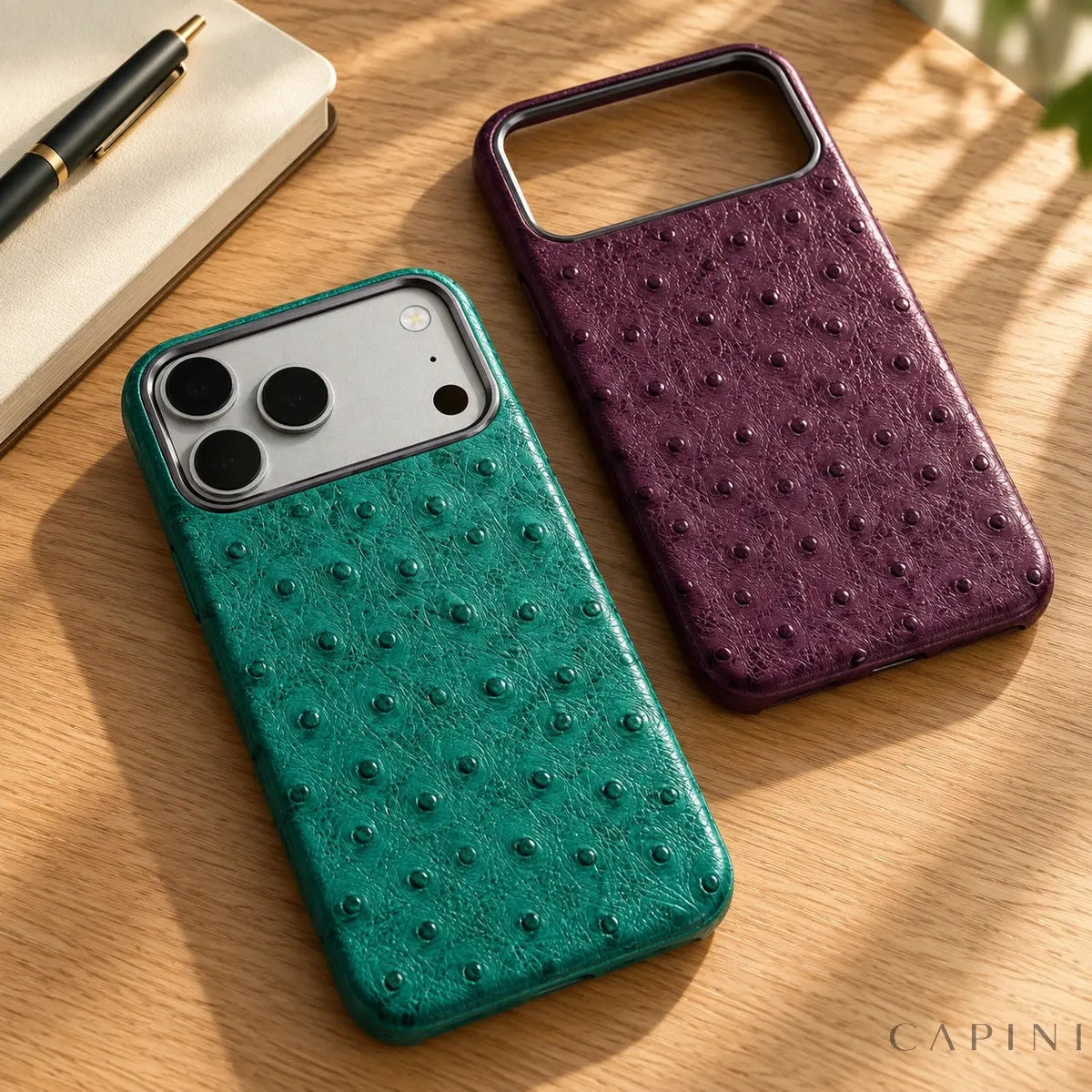 Teal Deruta case on a silver iPhone 17 Pro beside an empty Plum case on a clean writing desk; illustrative product photograph.