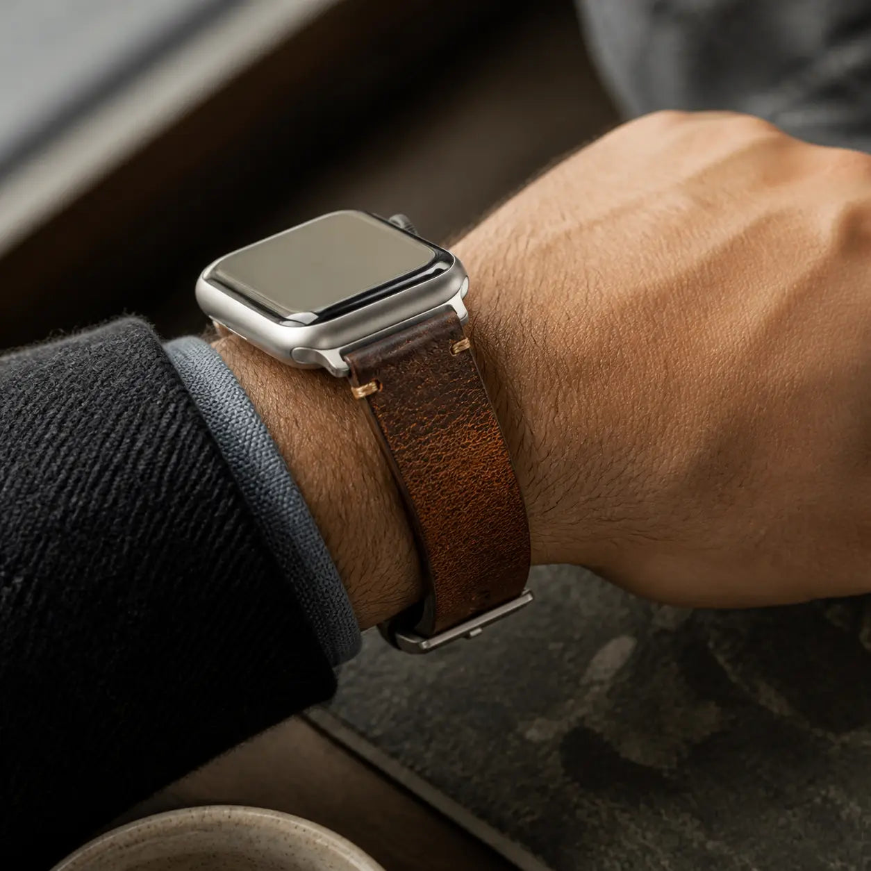 Antique brown Cremona Apple Watch strap with silver-tone hardware worn at a cafe