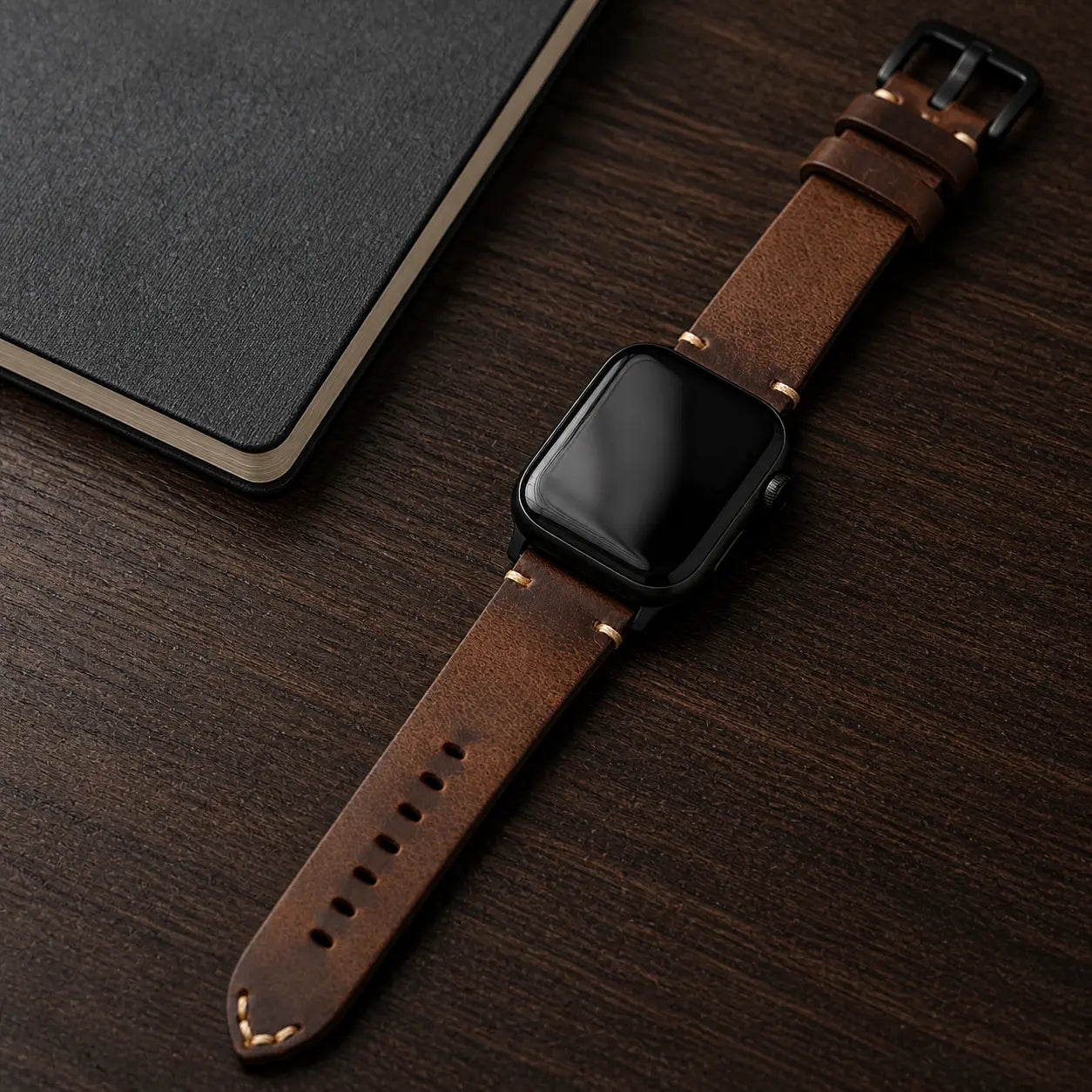 Antique brown Cremona Apple Watch strap with black hardware on a walnut desk