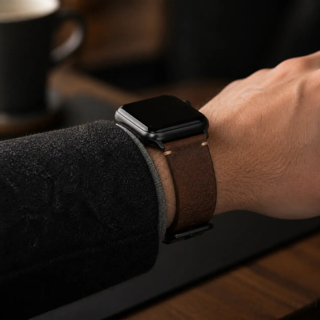 Antique brown Cremona Apple Watch strap with black hardware worn in a cafe
