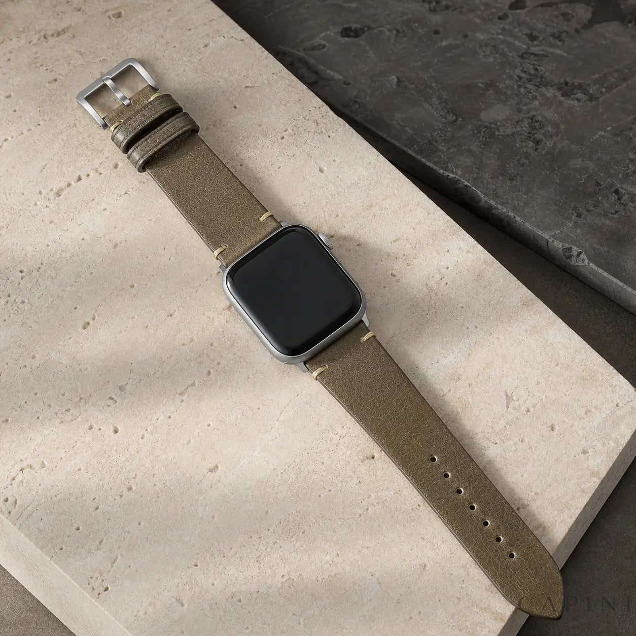 Gray Trieste oil-wax Apple Watch strap with silver hardware on travertine