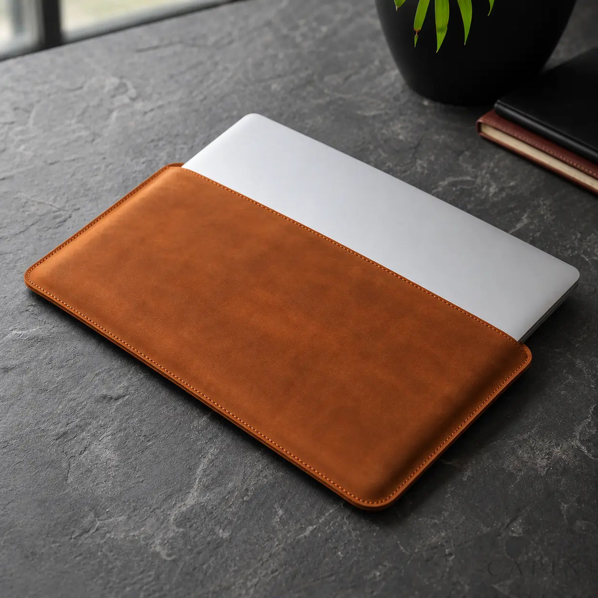 Closed silver laptop partly outside Pavia top long opening on dark stone