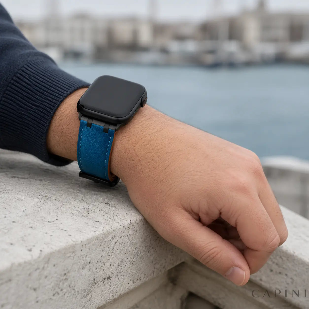 Ocean blue Terni Two-Tone Apple Watch strap with matte black hardware worn by the waterfront