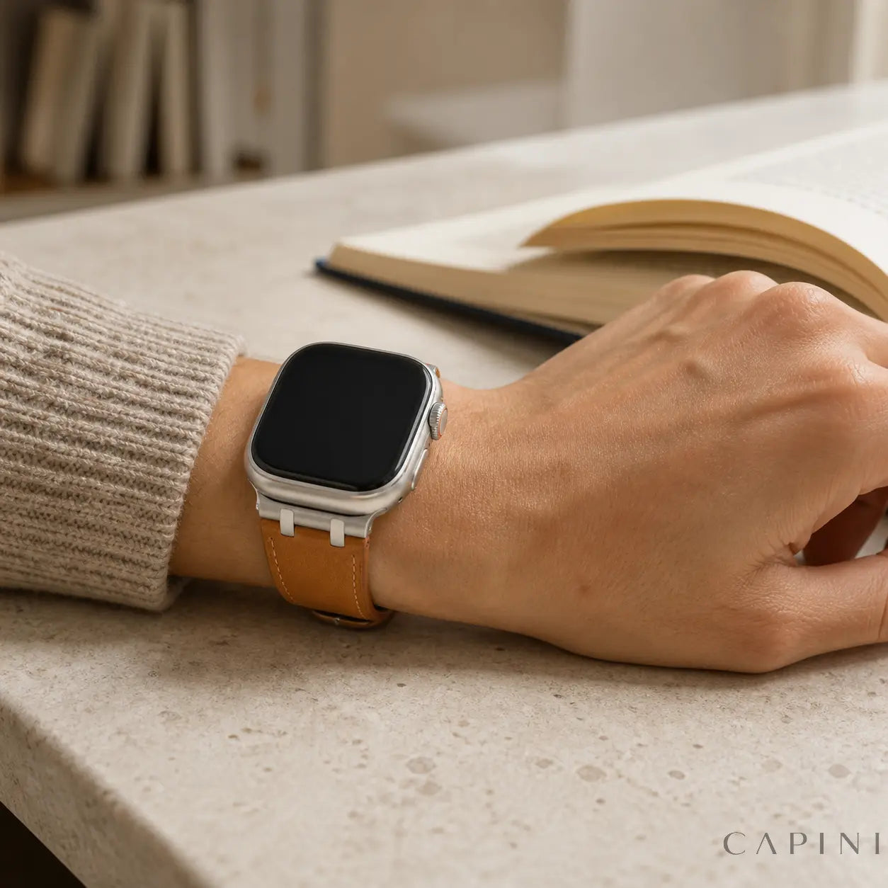 Tan Terni Two-Tone Apple Watch strap with titanium-tone hardware worn at a reading table